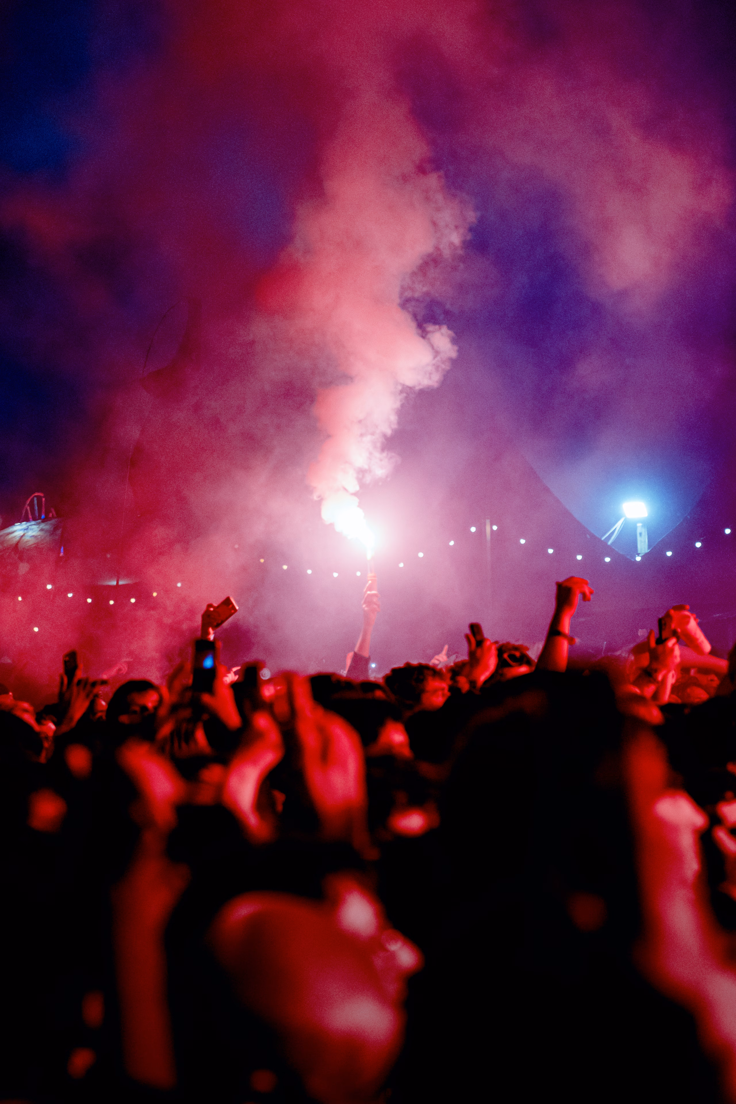 Foule de festival la nuit, bras levés autour d'un fumigène rouge