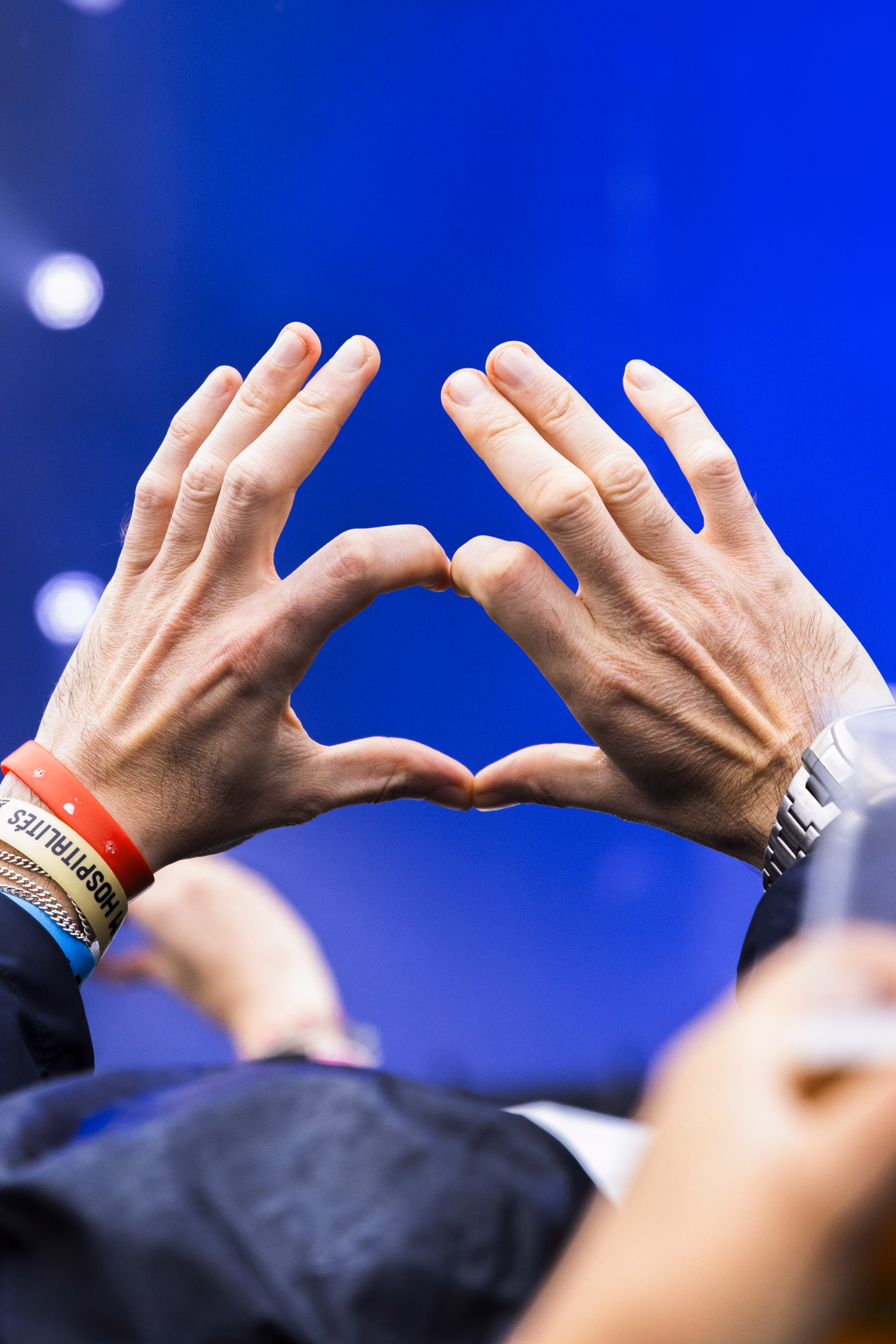 Deux mains formant un cœur au-dessus de la foule, bracelets de festival au poignet