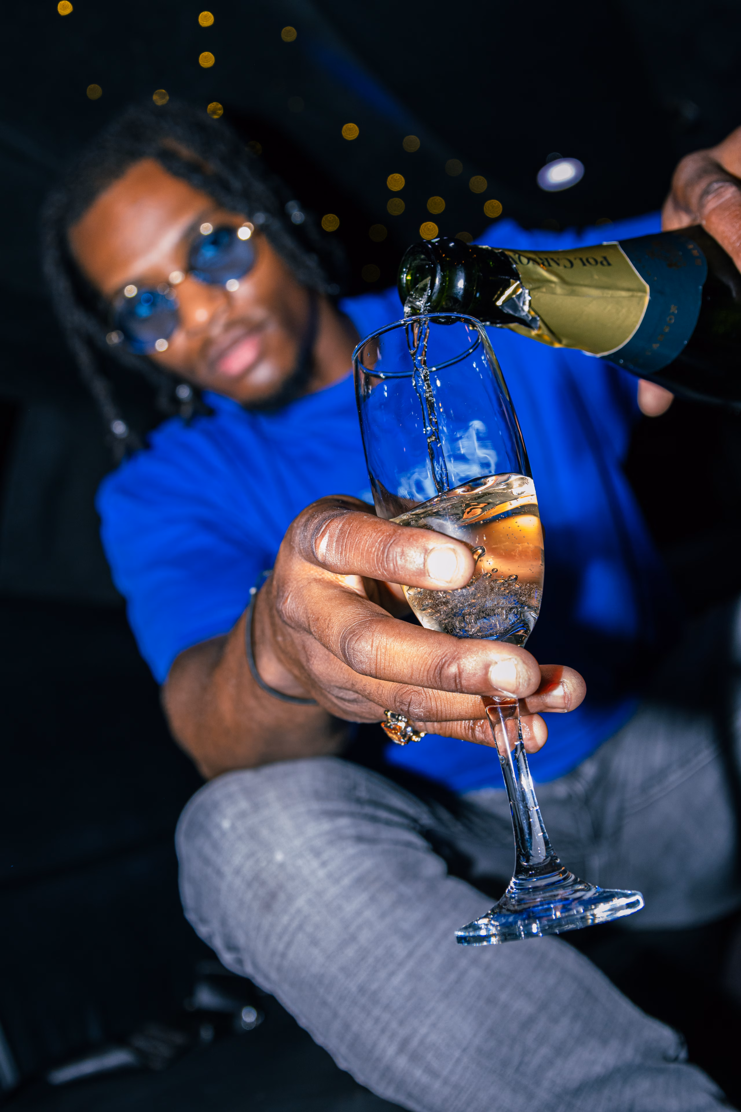 Champagne versé dans une flûte tendue par un homme à lunettes teintées, dans une limousine