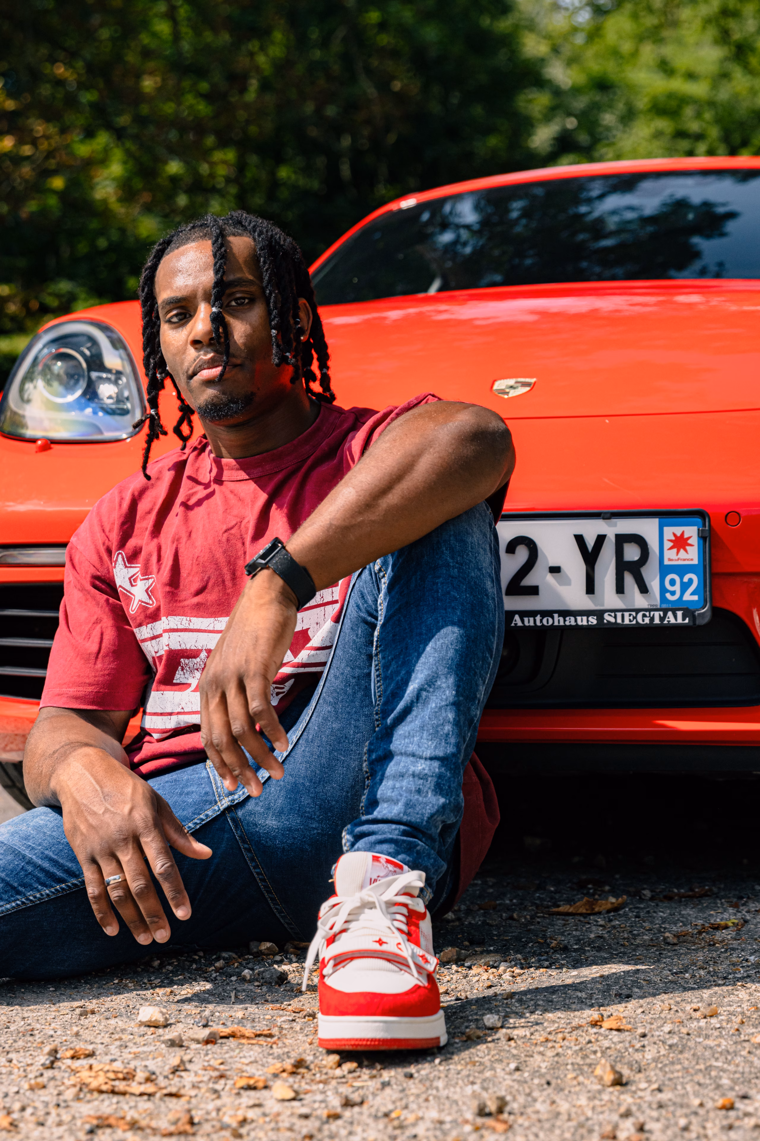 Homme assis au sol devant une voiture de sport rouge