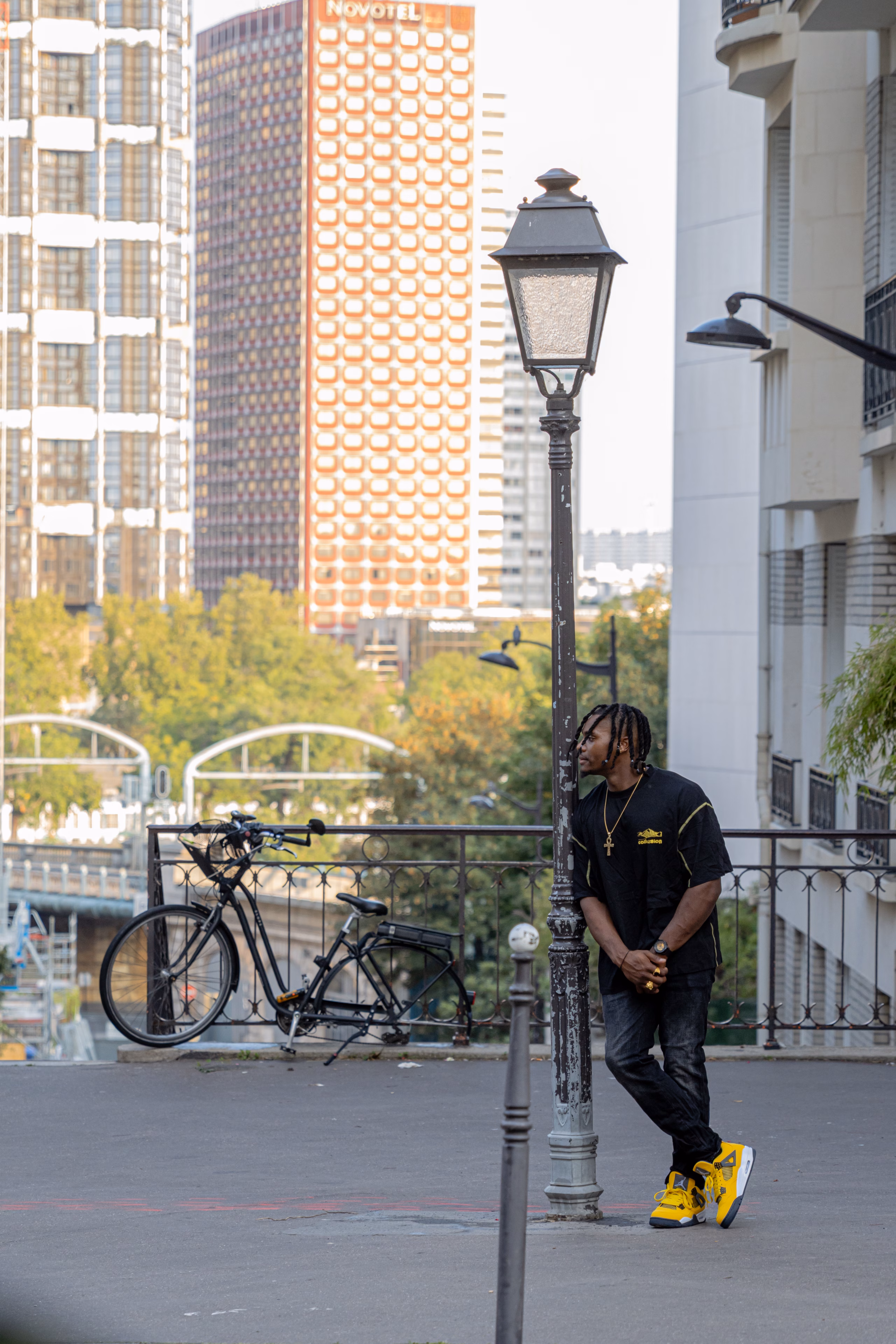 Homme adossé à un lampadaire parisien, vélo et tours en arrière-plan
