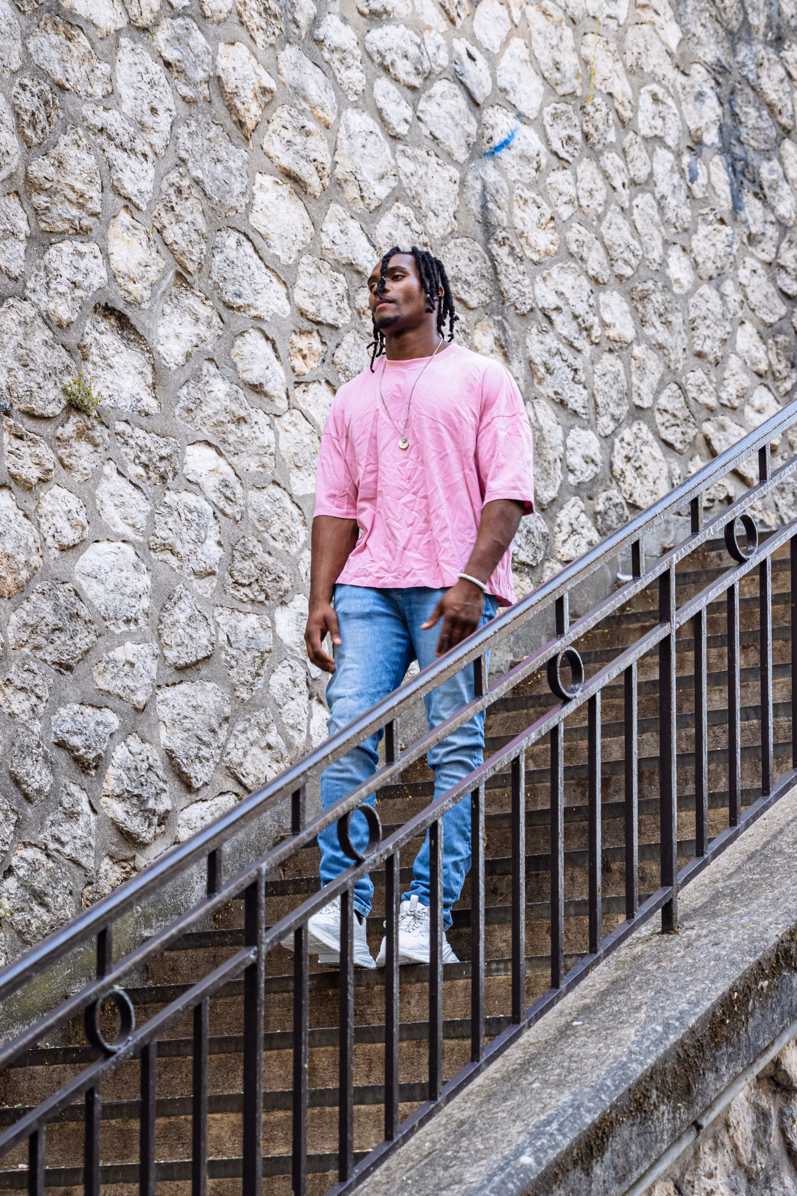 Homme en t-shirt rose sur un escalier extérieur le long d'un mur de pierre