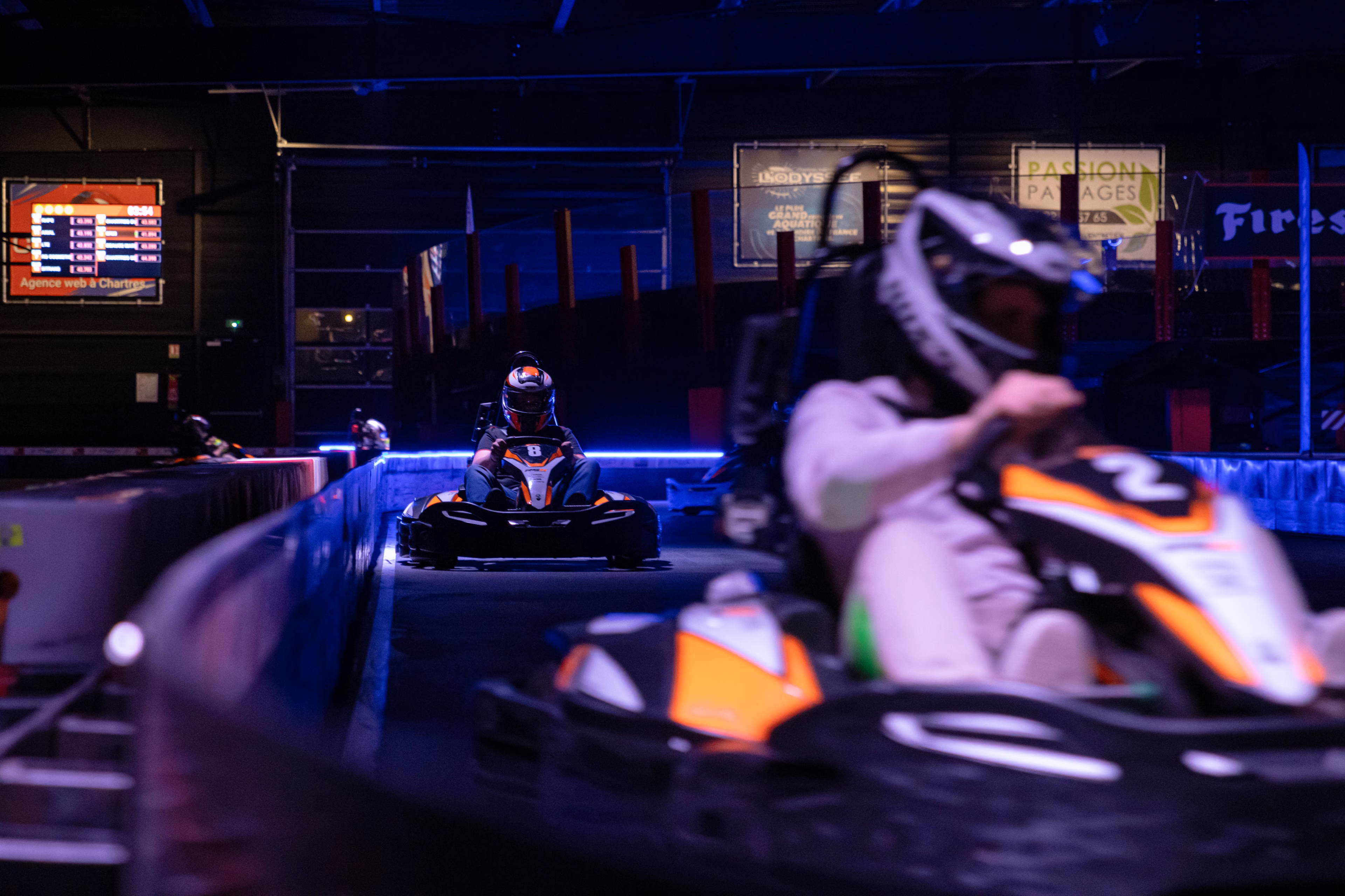 Kart au premier plan et concurrent en approche sur la piste d'un circuit couvert