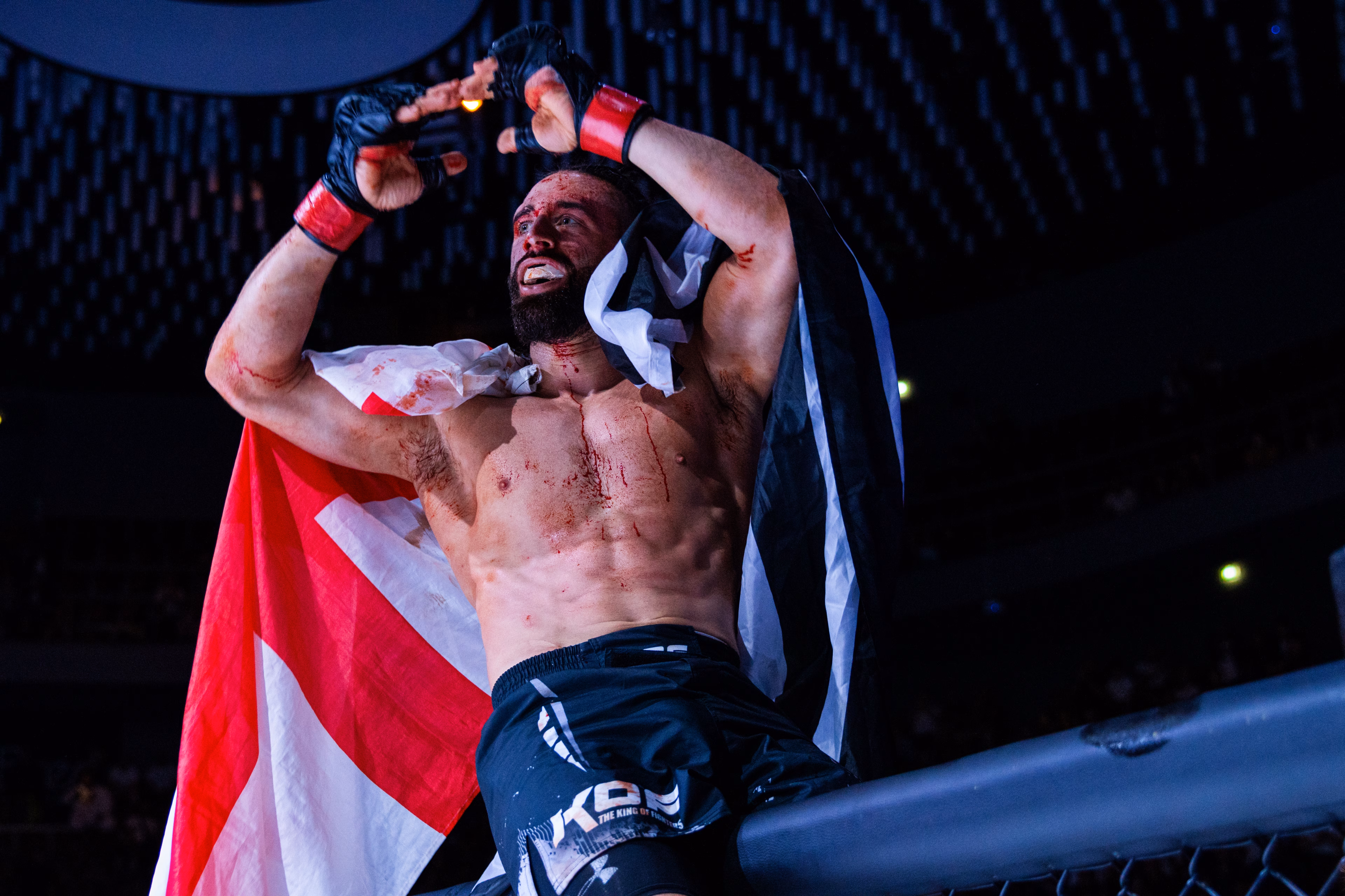 Combattant de MMA aux bras levés après sa victoire, un drapeau sur les épaules