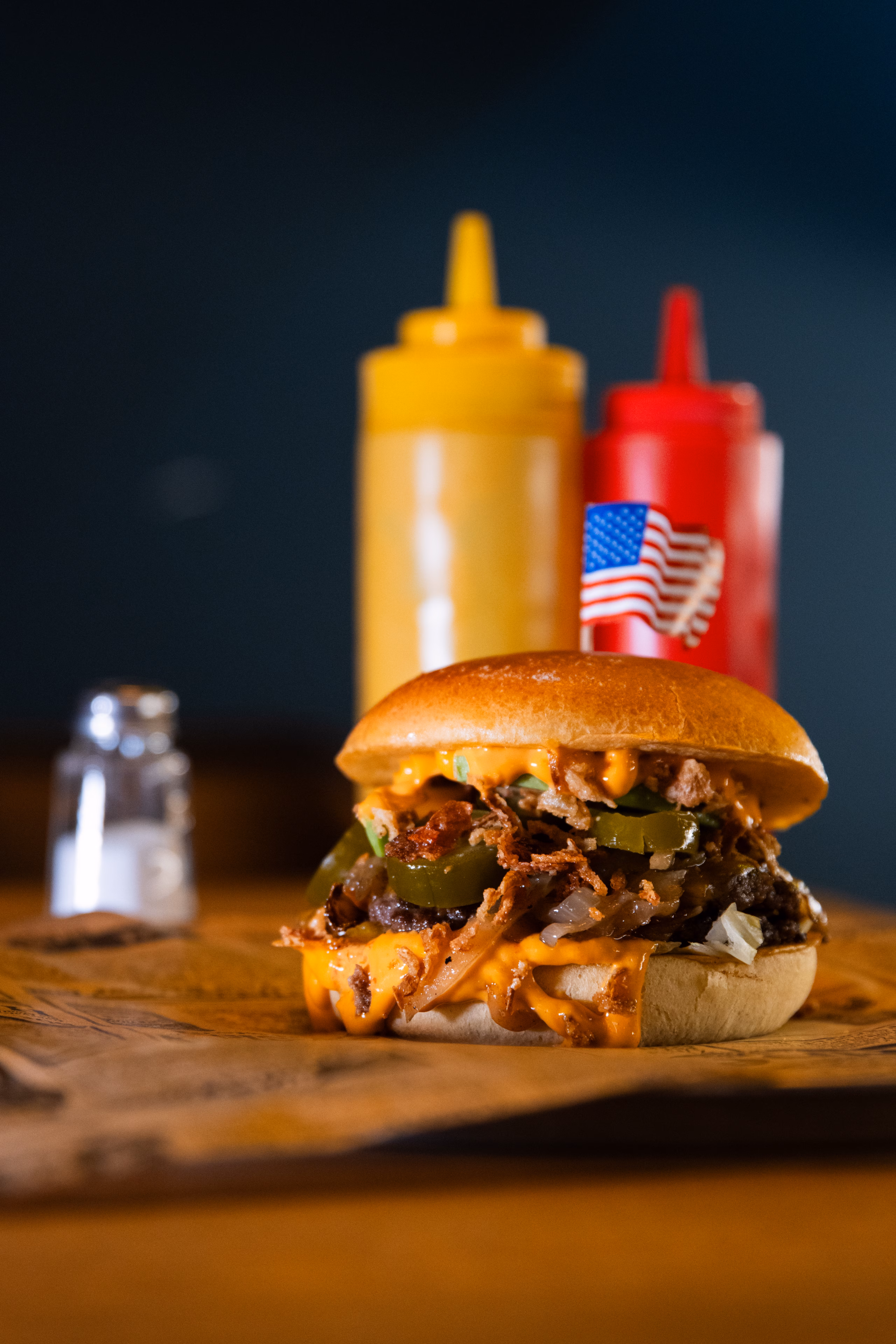 Burger aux oignons confits et cornichons, flacons de moutarde et de ketchup derrière