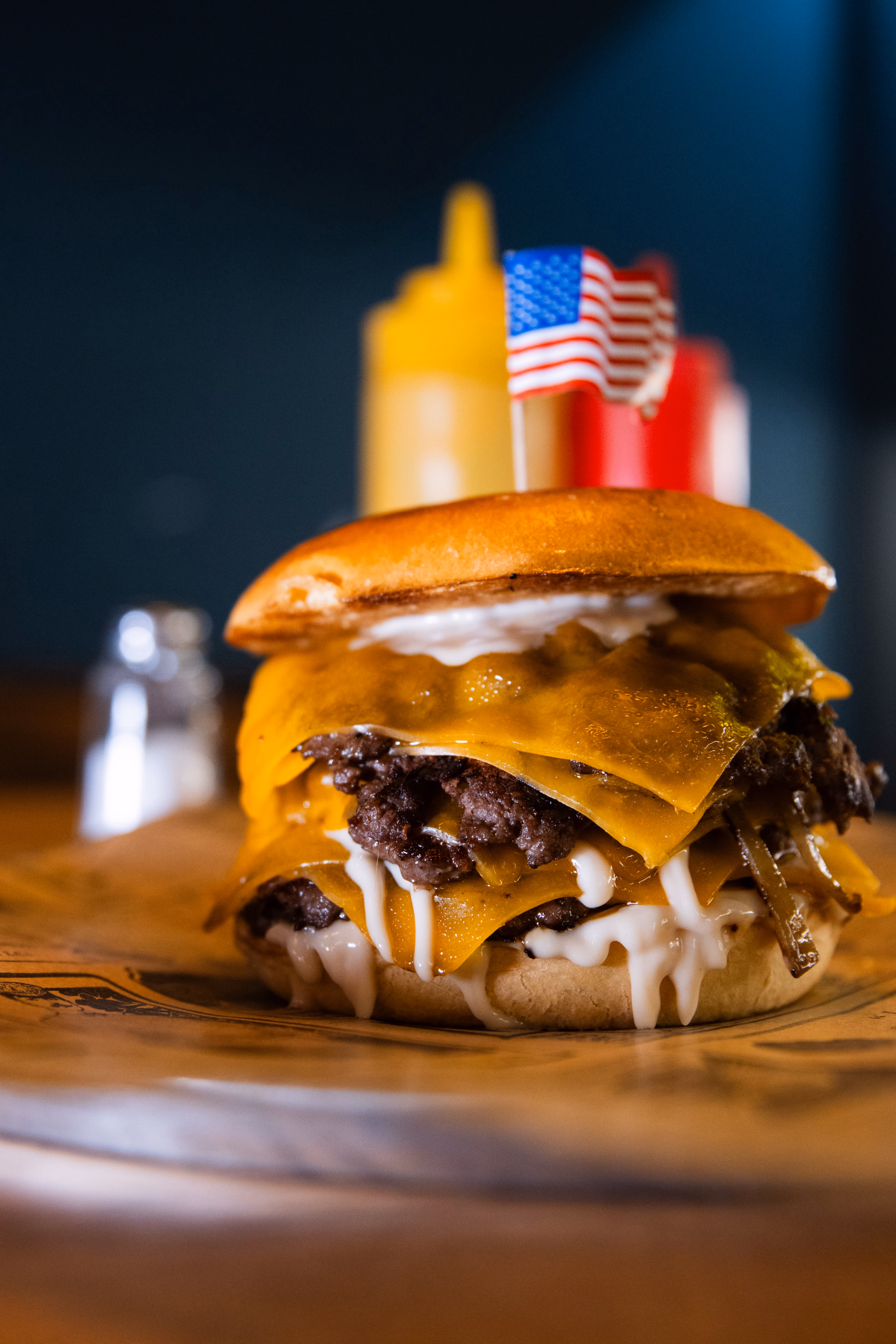 Double cheeseburger surmonté d'un petit drapeau américain, sur une planche en bois