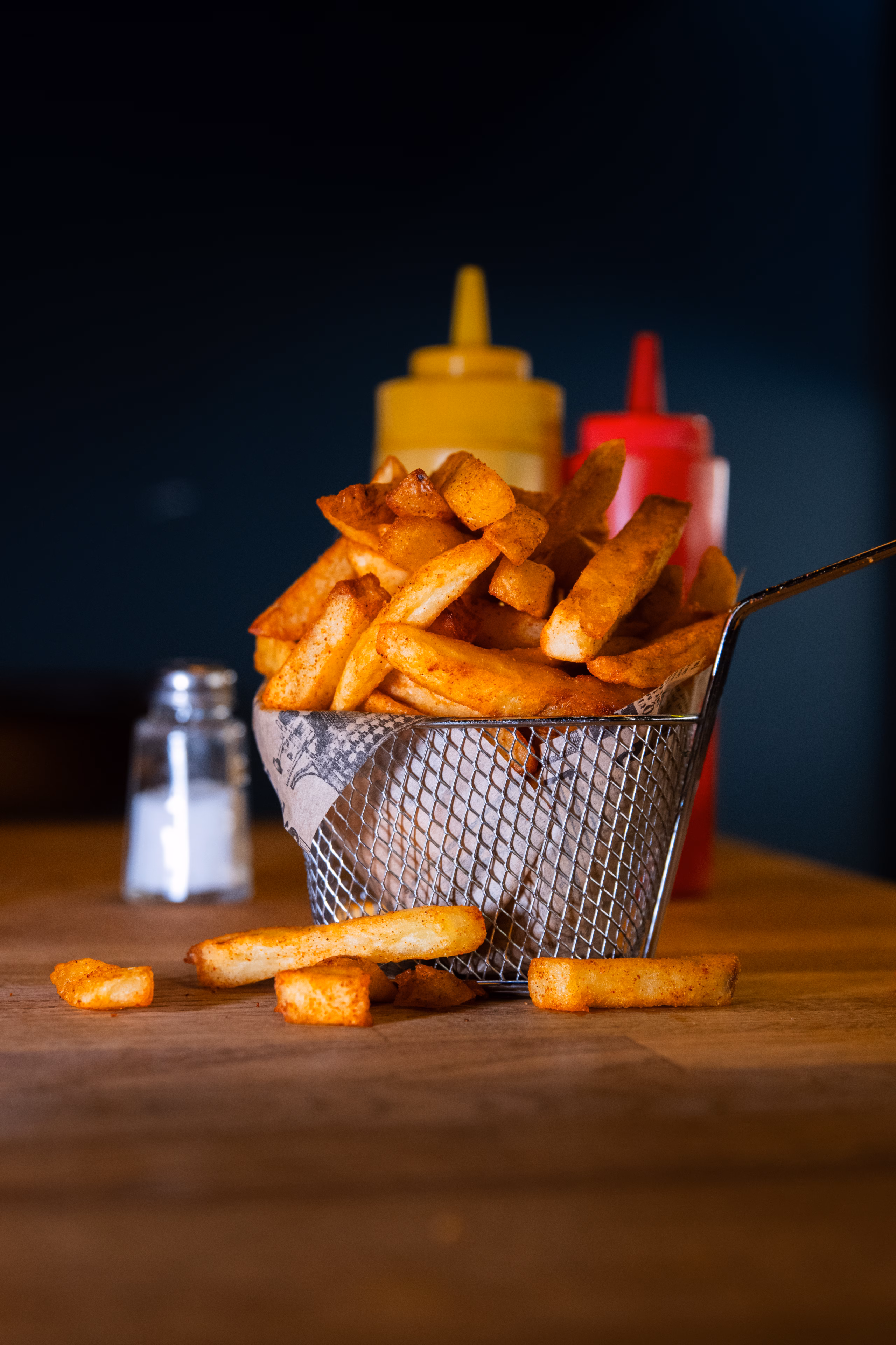 Frites assaisonnées servies dans un panier métallique sur une planche en bois