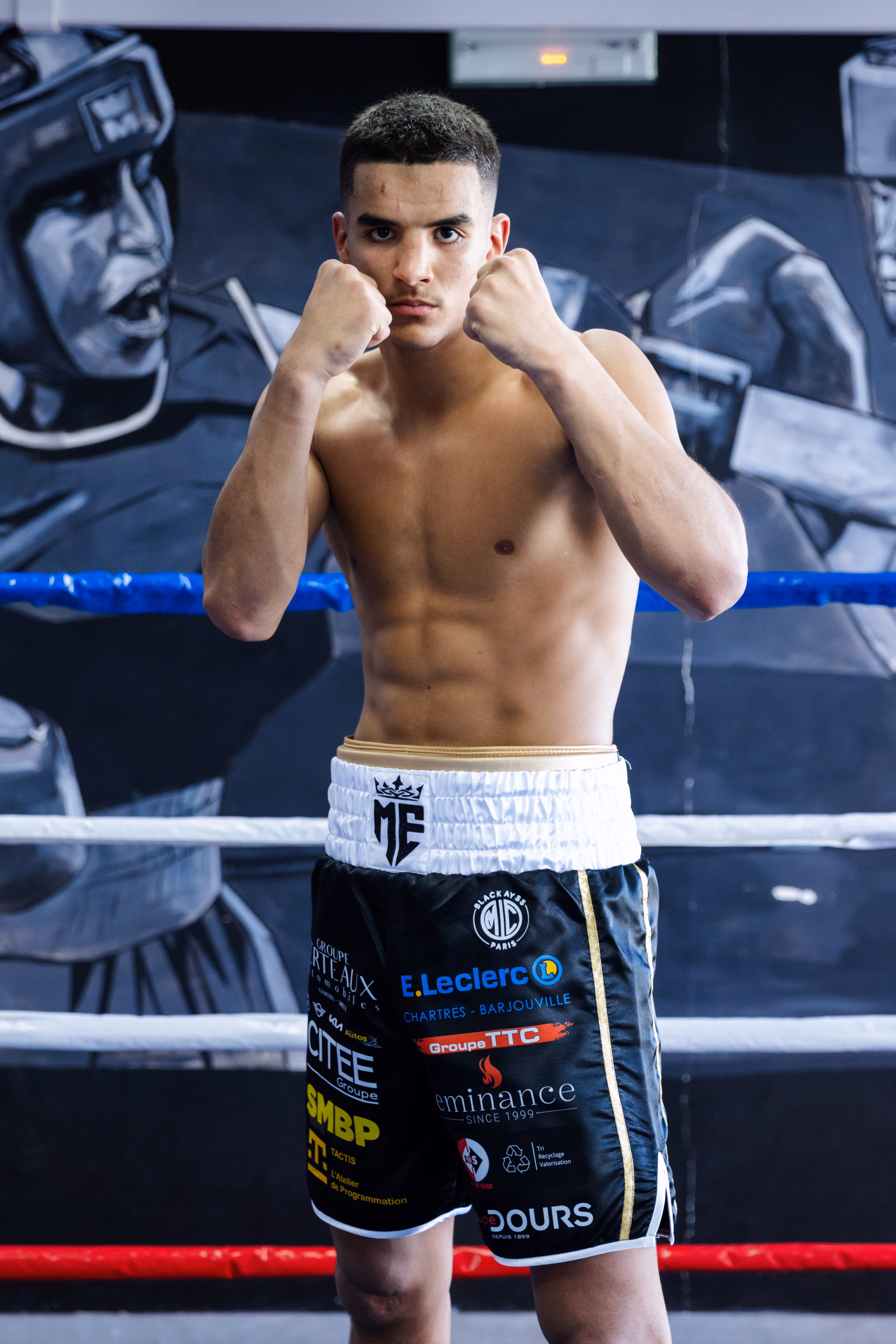 Jeune boxeur en garde sur le ring, fresque de boxeurs peinte derrière lui