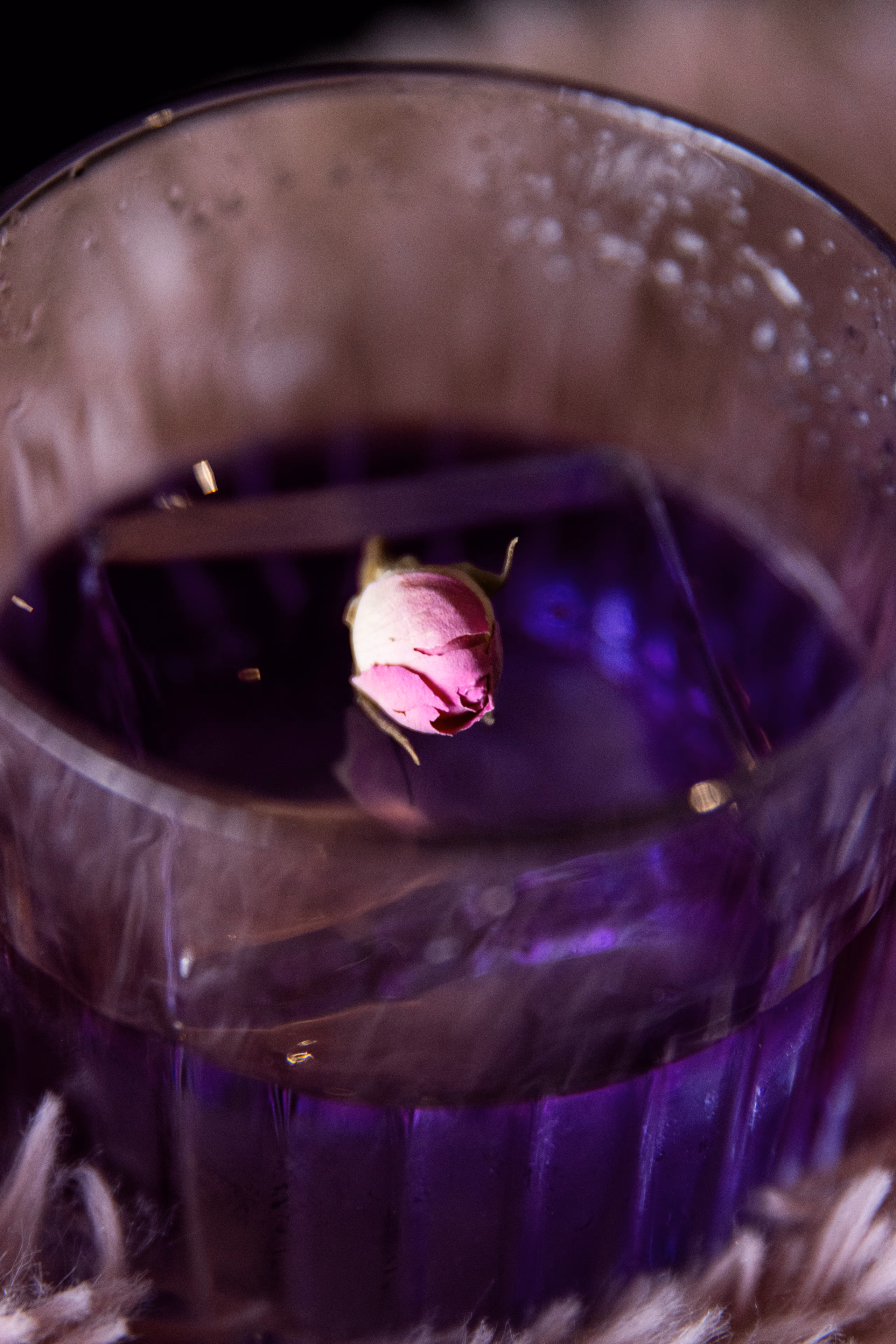 Cocktail violet dans un verre strié, un bouton de rose posé en surface